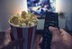 Person holding a cup of popcorn and a remote pointed at a television [Image by creator rcfotostock from AdobeStock]